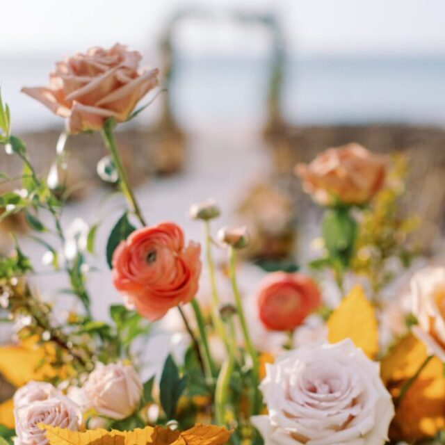 An arrangement of peach and orange flowers on the beach.