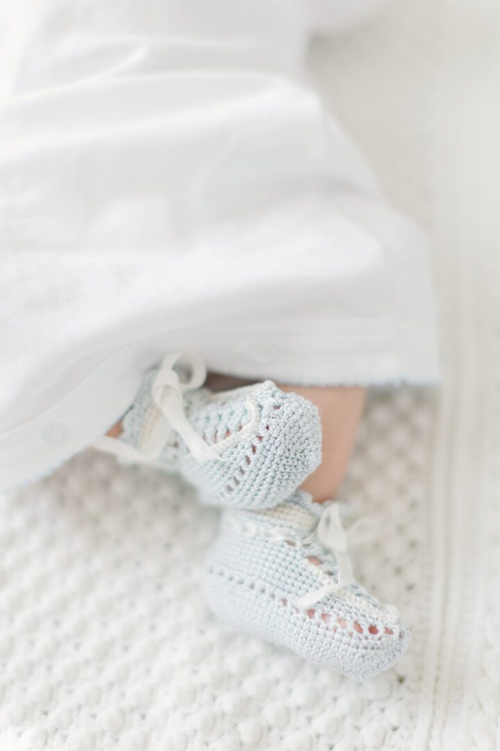 A baby is laying on a bed with blue crocheted shoes.