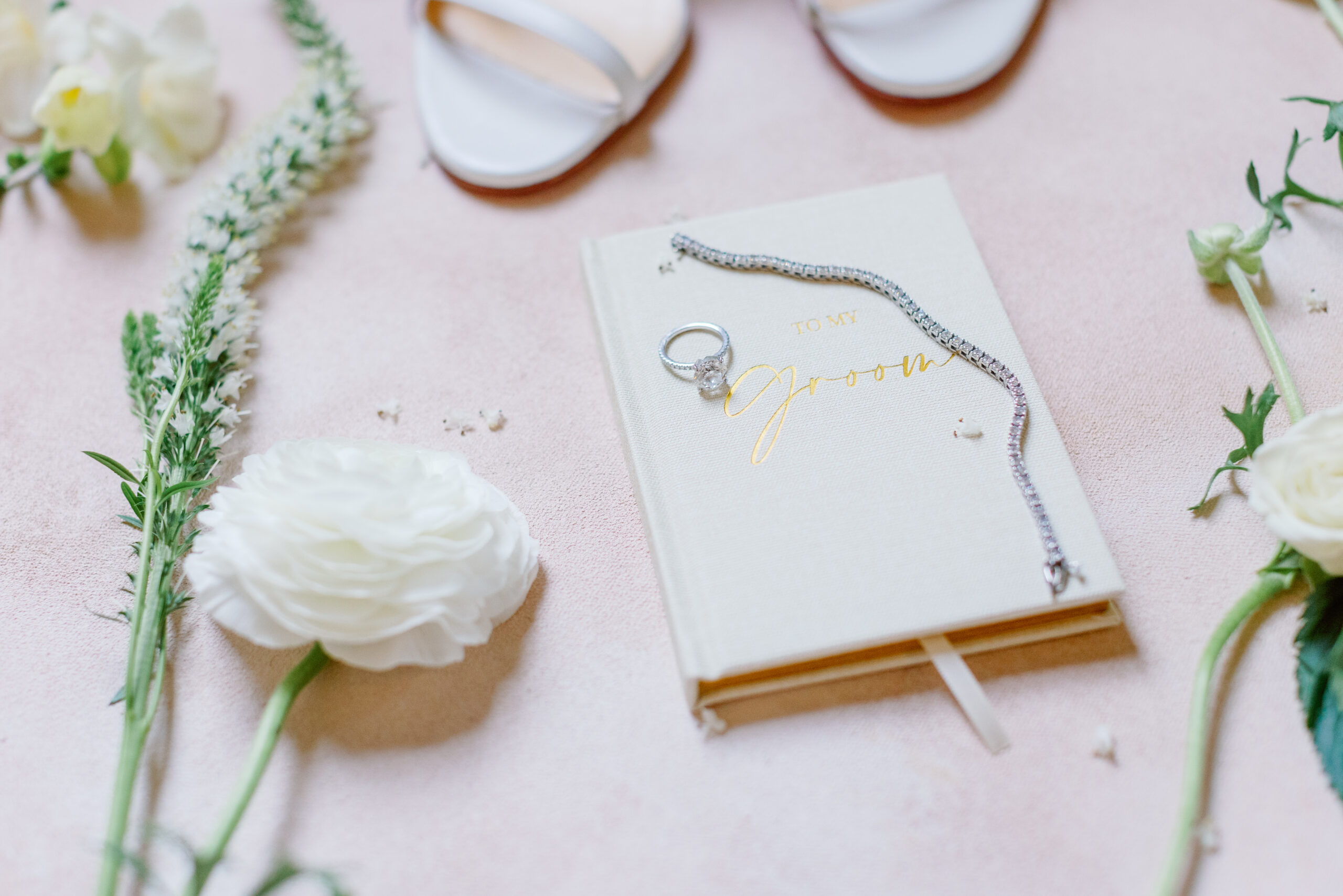 A wedding book, shoes and flowers on a pink background.