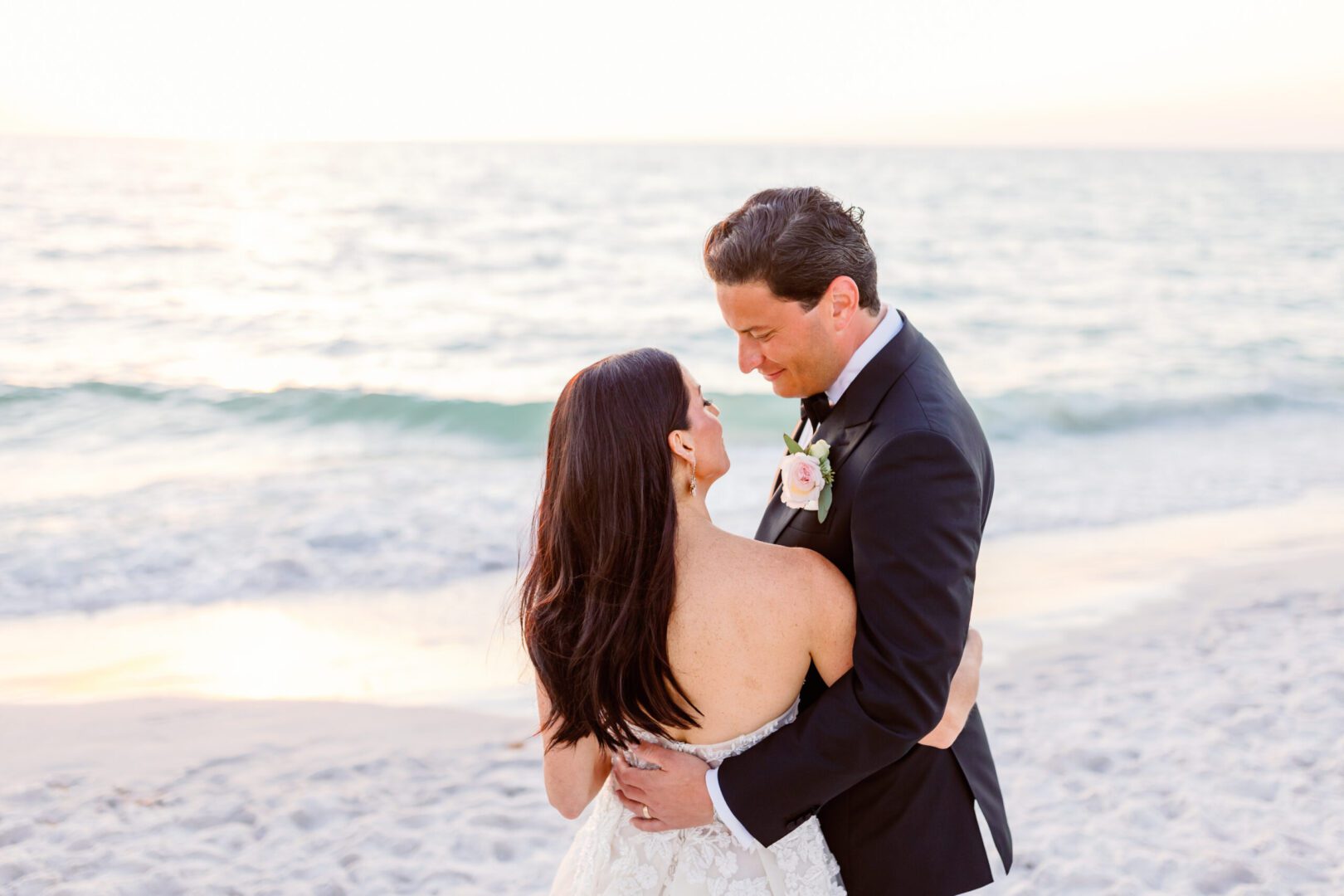 A bride and groom standing on the beach at sunset.